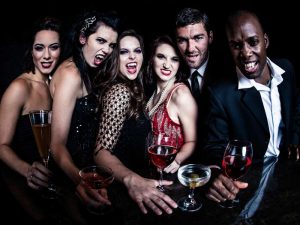 Party goers dressed in black and red baring fangs and drinking presumably alcoholic beverages.