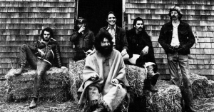 a black and white photo of the Grateful Dead from a promotional photoshoot. Jerry Garcia is sitting in front while other members stand behind him.