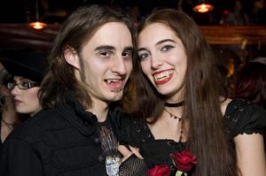 A man and woman wearing all black smiling and showing their fangs.