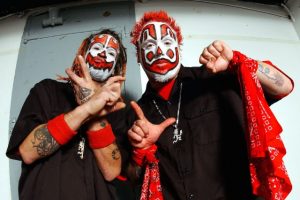 Photo of ICP members Shaggy 2 Dope and Violent J in clown makeup, died red hair, and black and red outfits. They are holding up piece signs and fists.