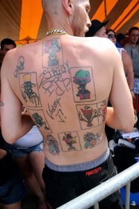 In this photo, a man's back is facing the camera. He has nine Juggalo Joker tattoos, each in different colors. 