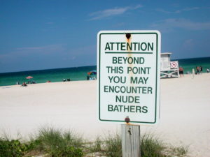 Sign at a nude beach reading: Attention: beyond this point you may encounter nude bathers.