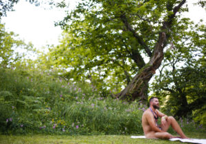 Image of a nudist man relaxing by a tree