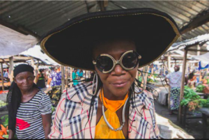Musa Umpalaba smiles into the camera while at the local market, next to a woman who is dressed in simple clothes