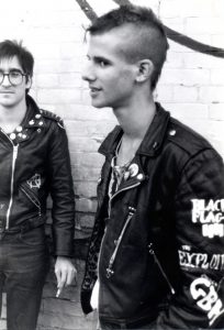 Two punks standing on a corner in black jackets with custom embroidery and buttons.