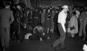 This image shows a pachuco on the ground, being stripped of his clothing and being beaten. There are numerous people watching this take place.