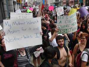 An image of people walking in a Women's March. Many are holding signs supporting anti-rape statements.