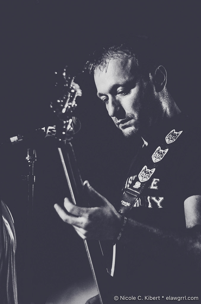 A photo portrait of musician Jeff Rosenstock, looking down at his guitar in front of a mic in grayscale