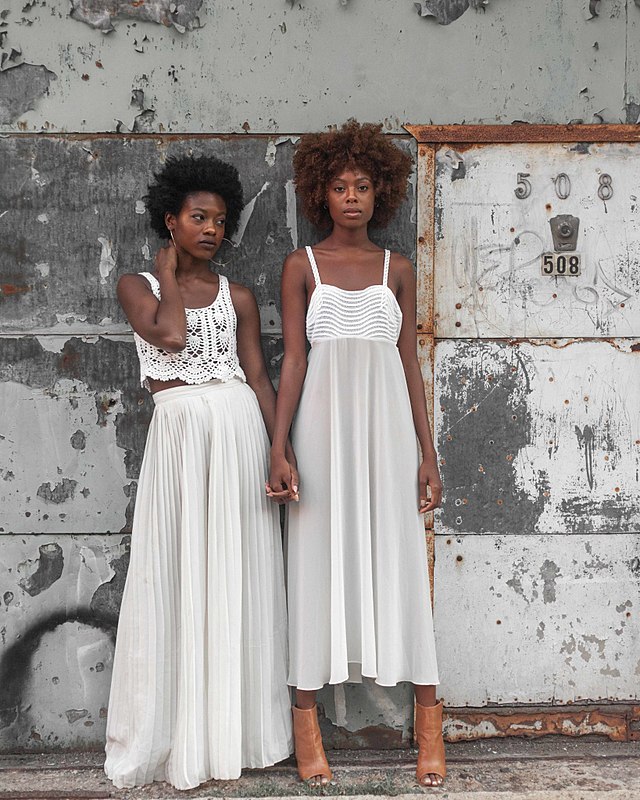 Two women in white, loose skirts are pictured holding hands