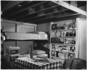 A small underground shelter with bunk beds, a table and chairs, and supplies, including a first aid kit, books, and food.