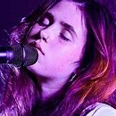 Indie Singer/Song writer Clairo at a performance, eyes closed and head upturned in front of a mic