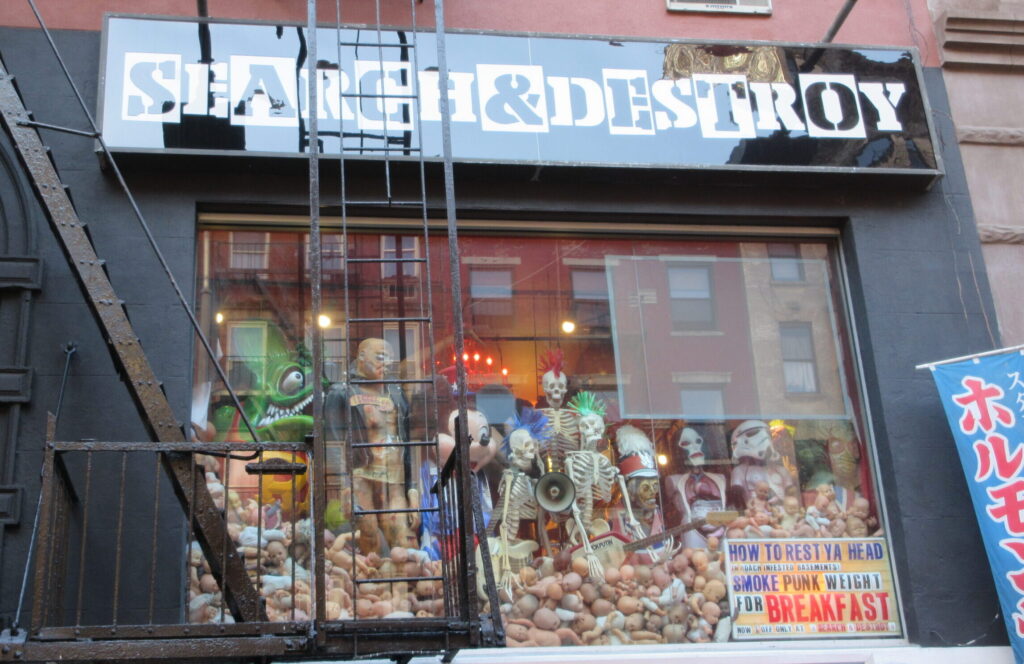 The outside of a secondhand clothing/punk store called Search & Destroy. The windows have dolls and skeletons with mohawks.