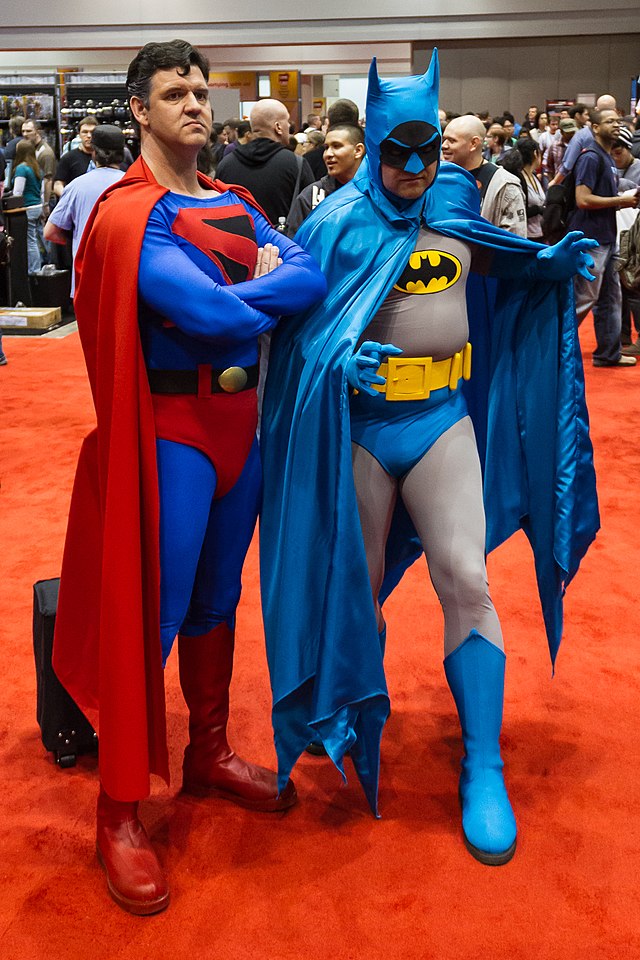 Two adult men dressed as Superman and Batman posing for a picture