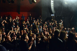 A group of people at a metal concert. Many are dressed in black and have their hands raised above their heads.