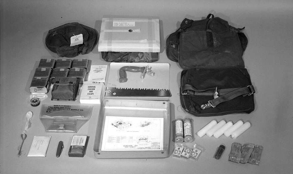 A bag and survival gear, including a pocketknife, saw, matches, and other items that are difficult to identify.